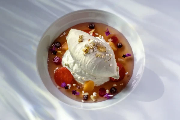 Dessert mit Blüten und Fruchtsauce auf einem weißen Teller angerichtet