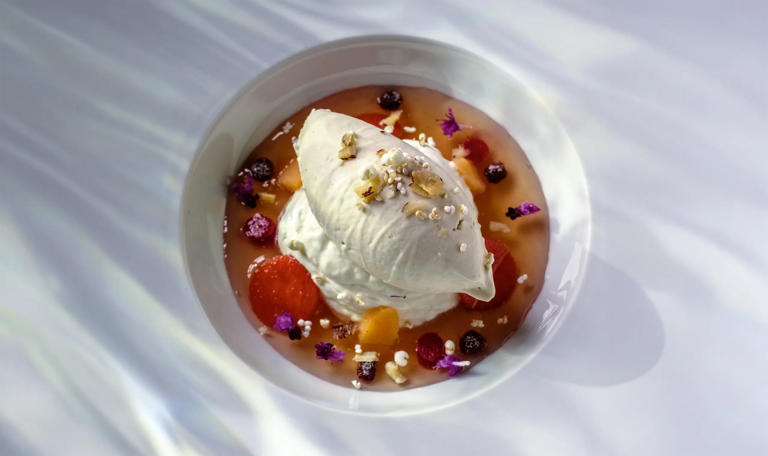 Dessert mit Blüten und Fruchtsauce auf einem weißen Teller angerichtet
