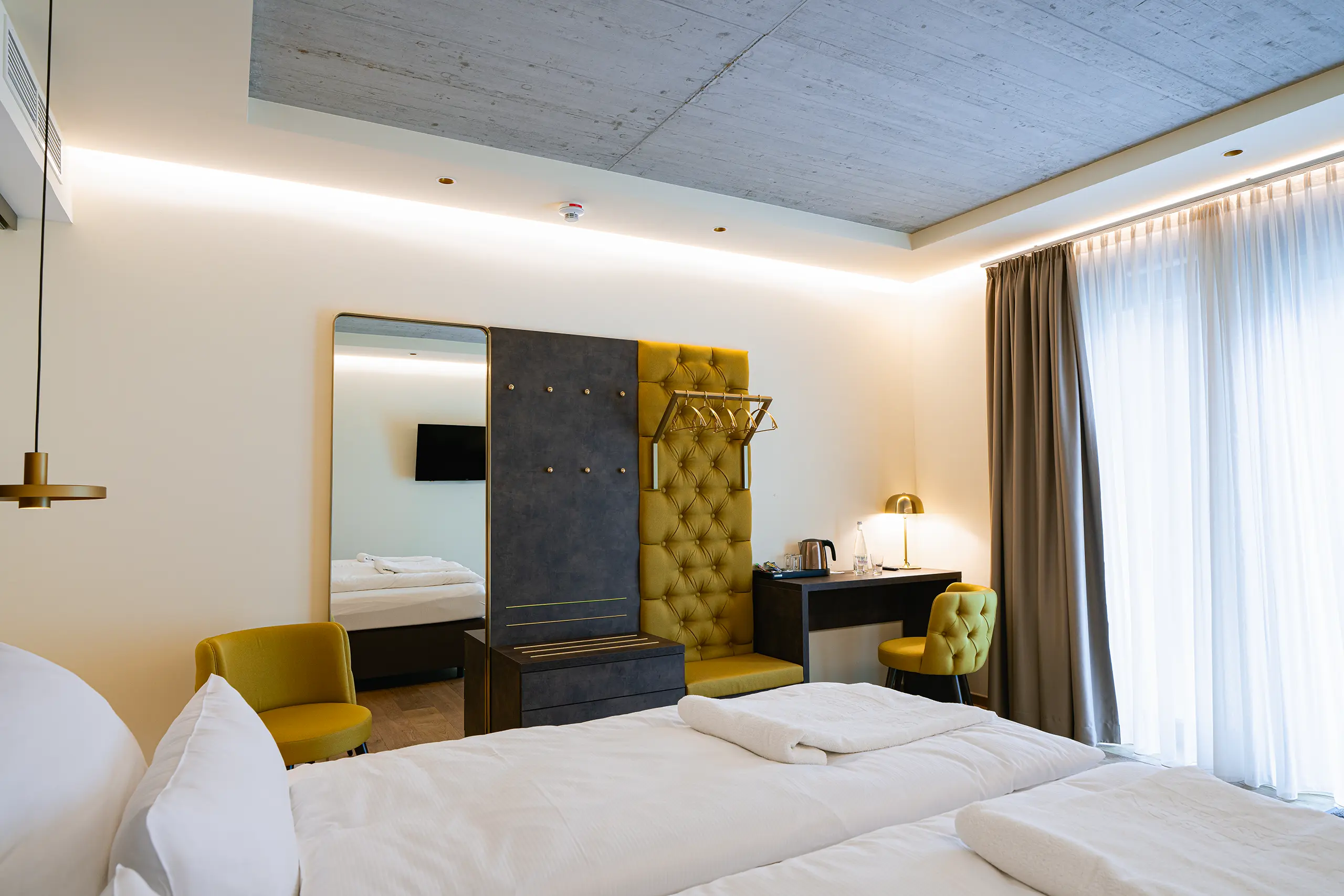 Superior-Zimmer 22 im Neubau mit Doppelbett, Sichtbetondecke und gelbem Sessel