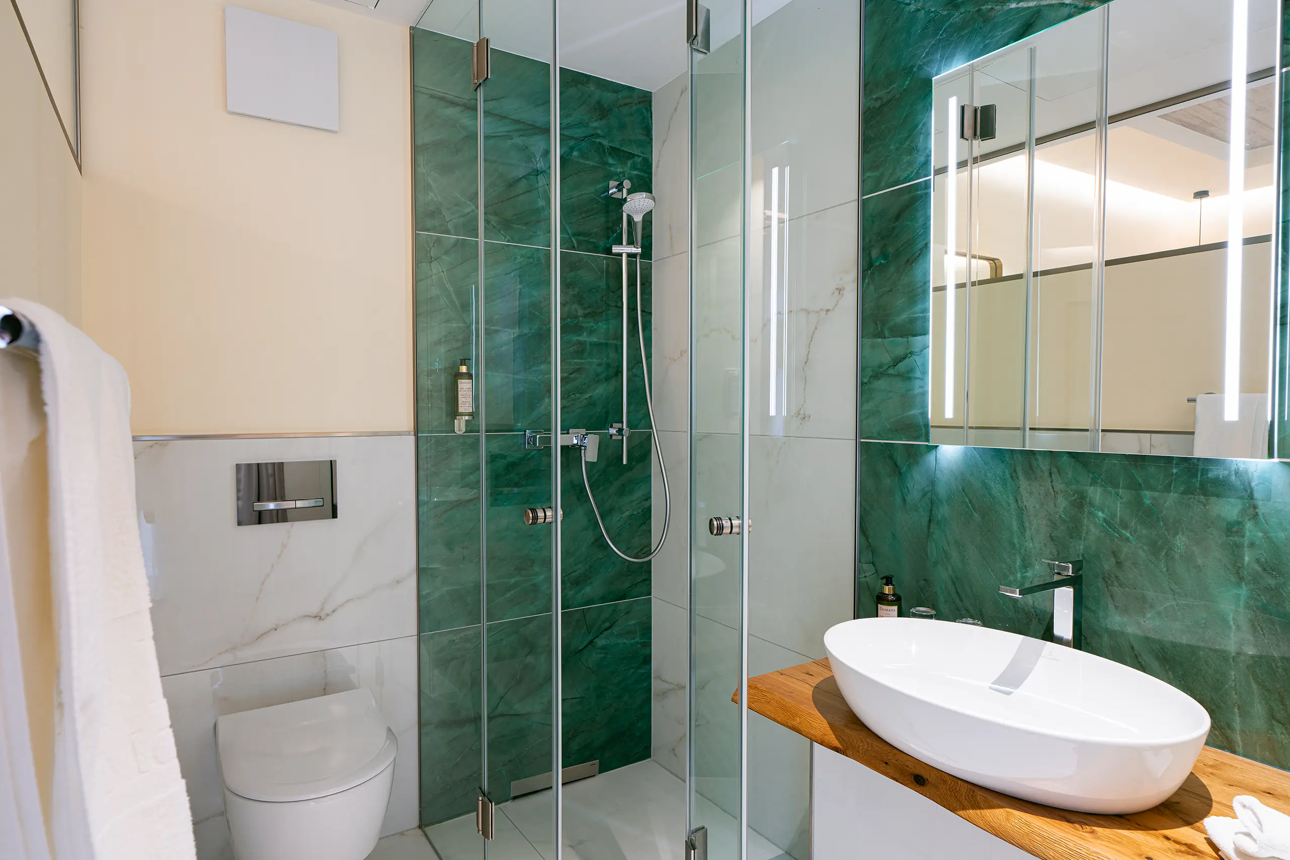 Badezimmer in Zimmer 23 im Neubau mit Waschbecken, Spiegel und grüner Marmordusche