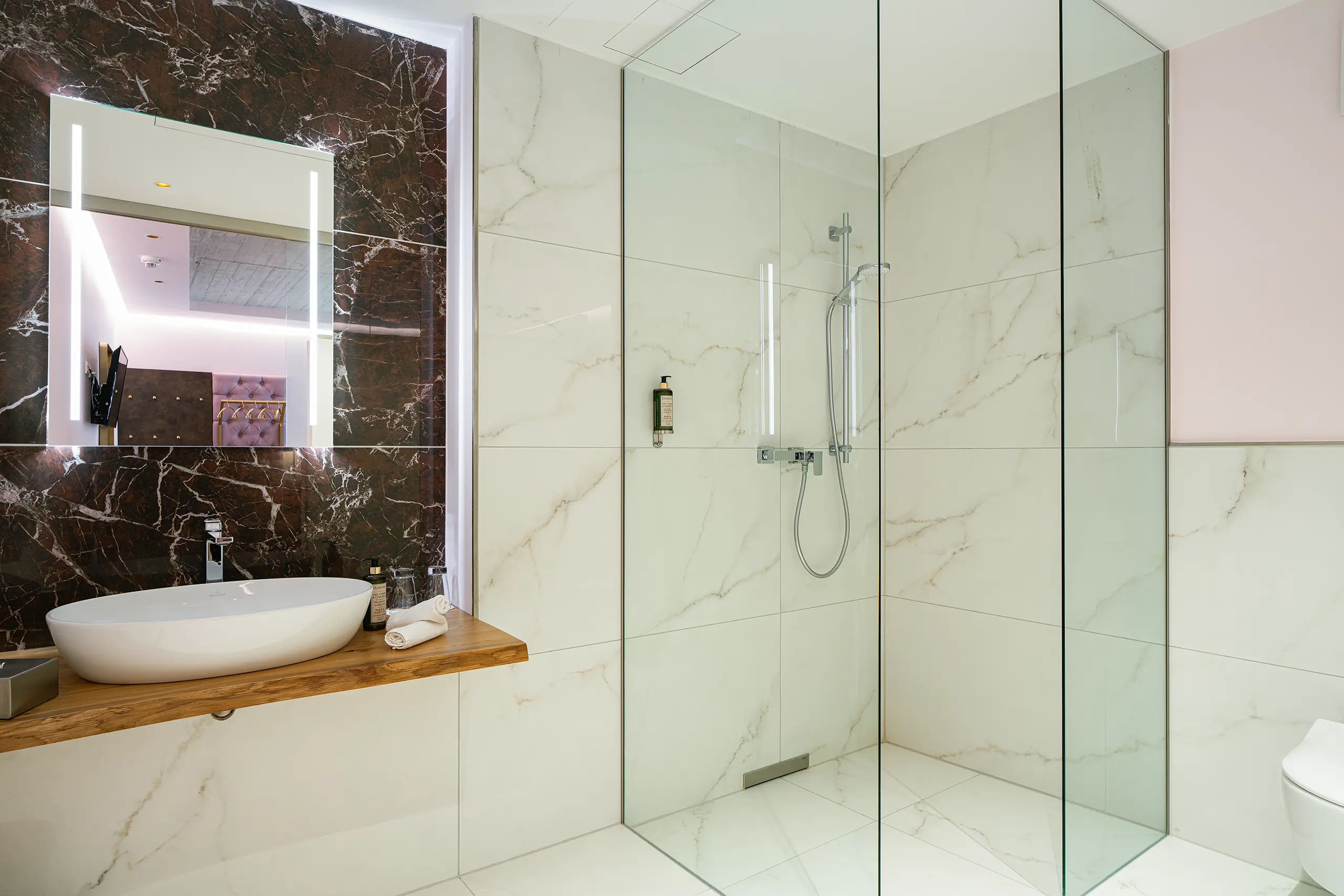 Badezimmer in Zimmer 24 im Neubau mit dunkler Marmorwand und Glasdusche