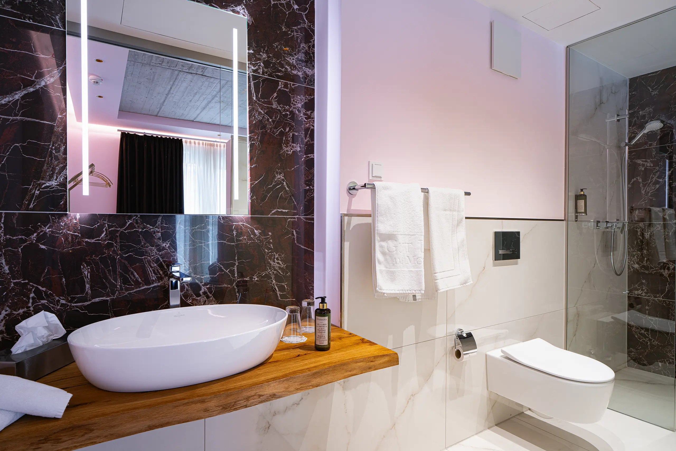 Badezimmer in Zimmer 25 im Neubau mit Waschbecken auf Holzplatte und Marmorwand