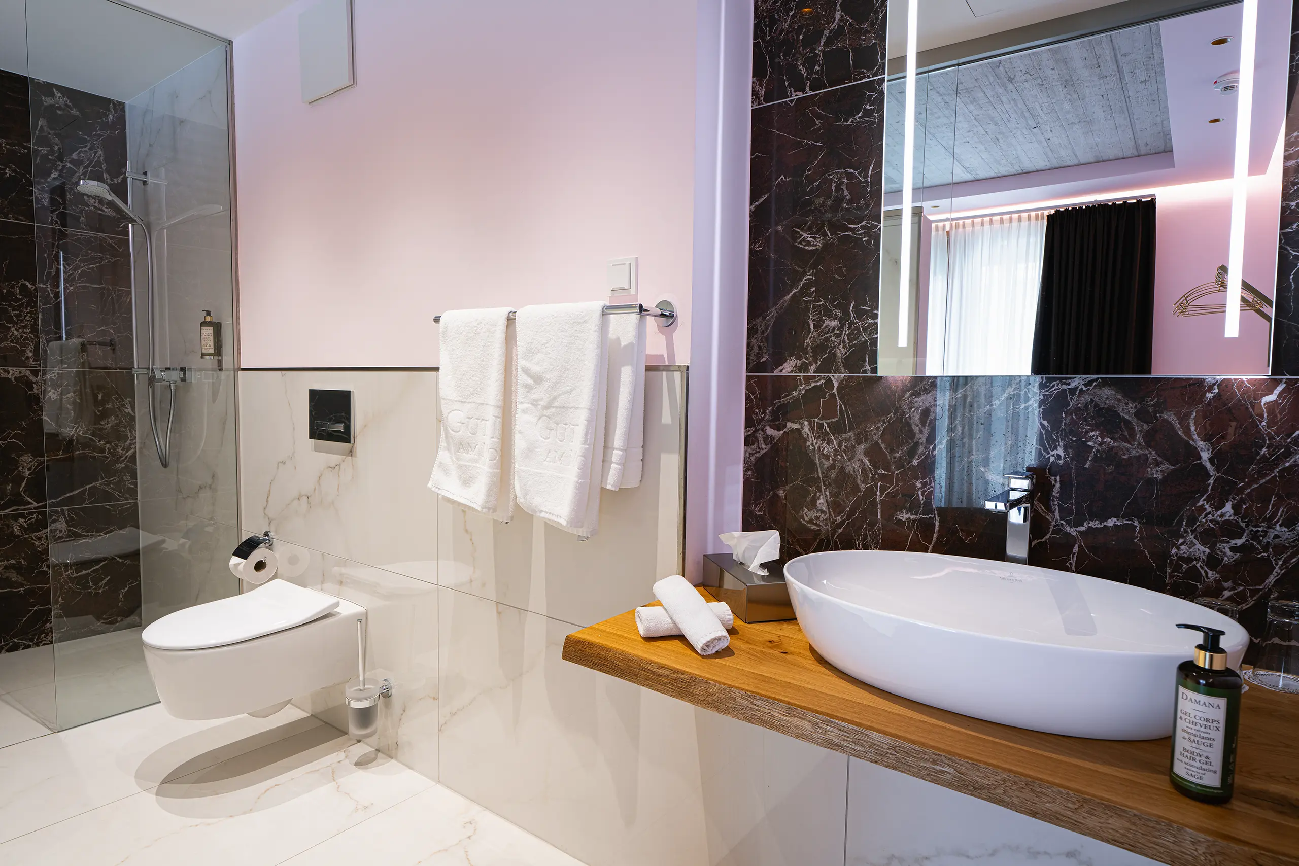 Badezimmer in Zimmer 26 im Neubau mit Waschbecken, dunklem Marmor und Dusche
