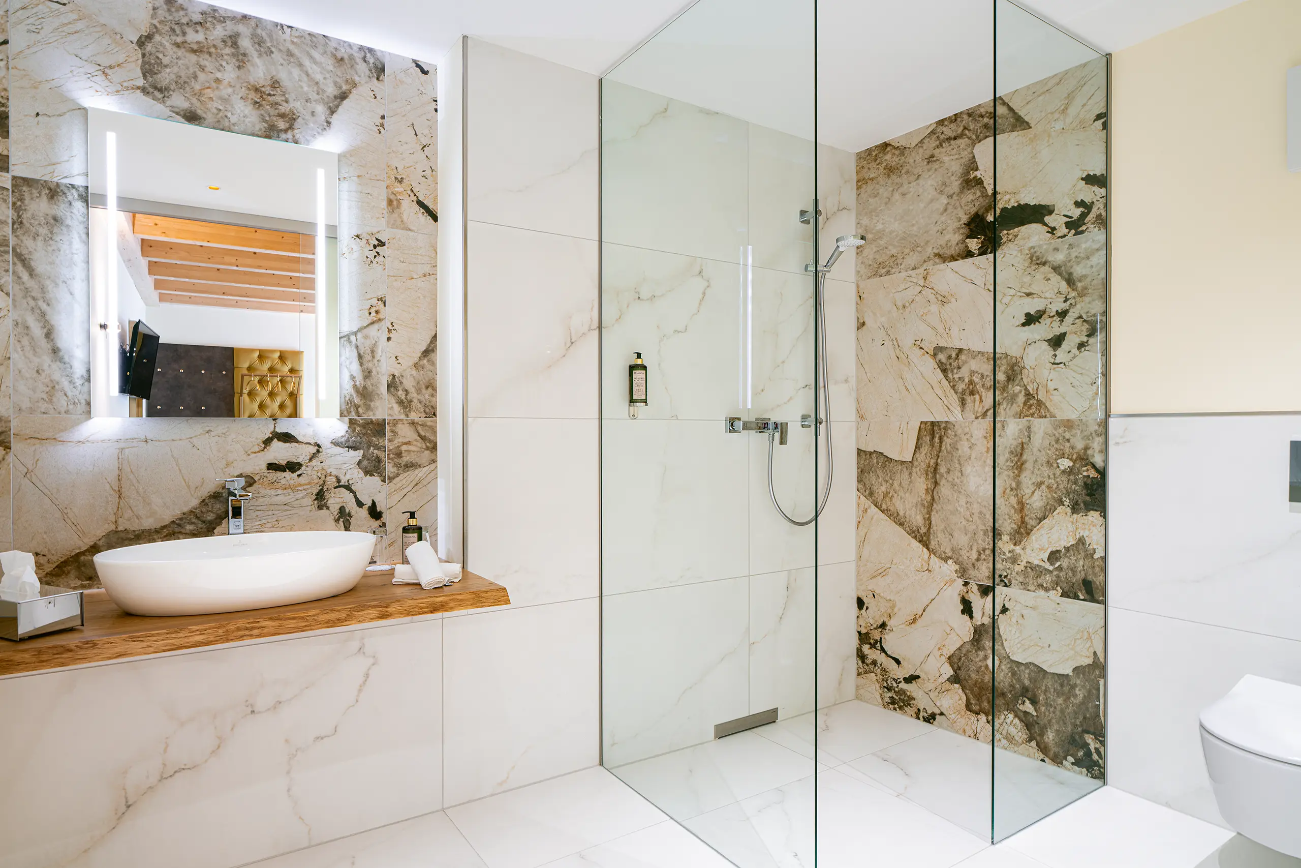 Badezimmer in Zimmer 28 im Neubau mit Marmorwand, Glasdusche und Waschbecken