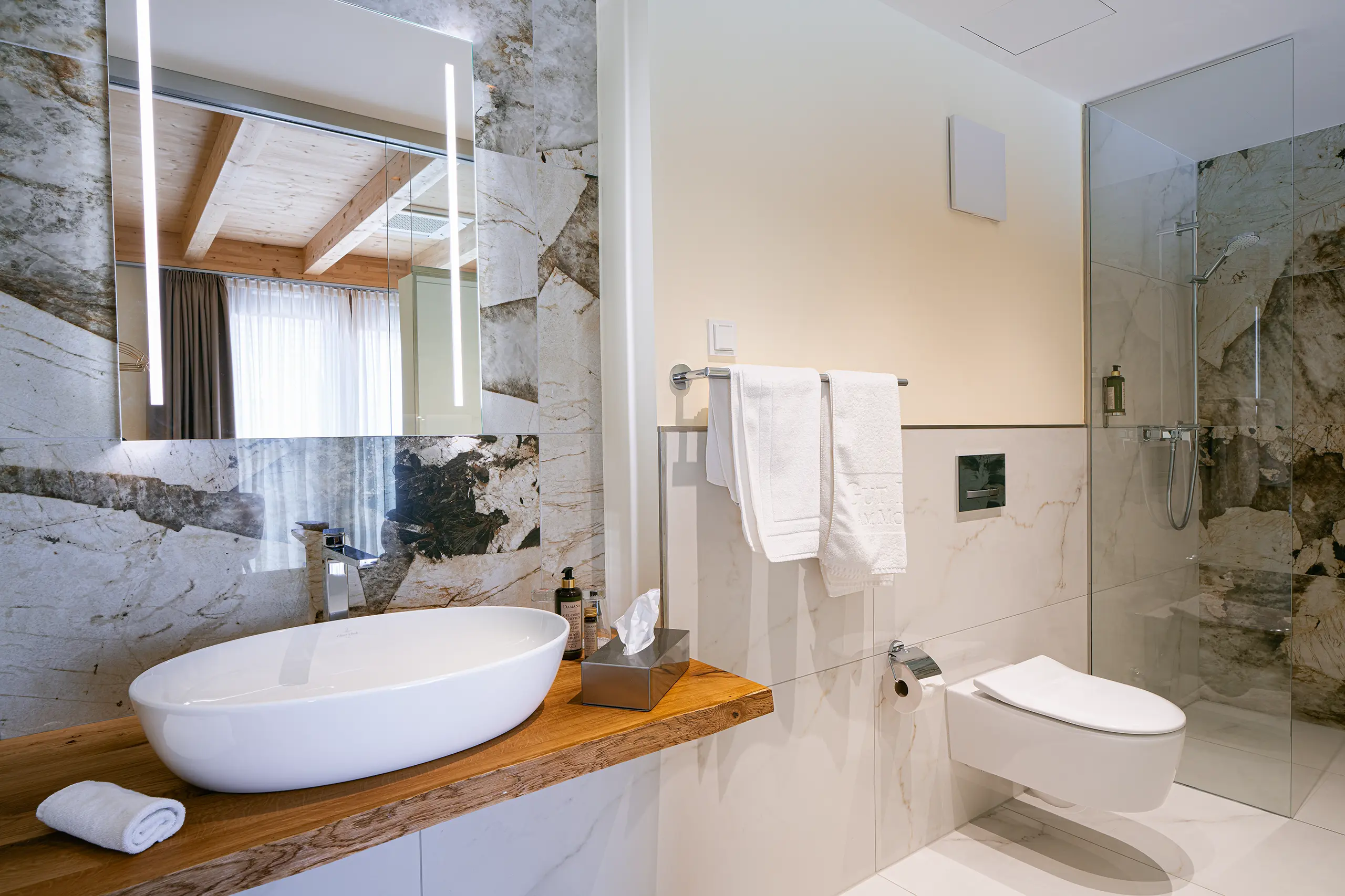 Badezimmer in Zimmer 29 im Neubau mit Waschbecken, Marmorwand und Glasdusche