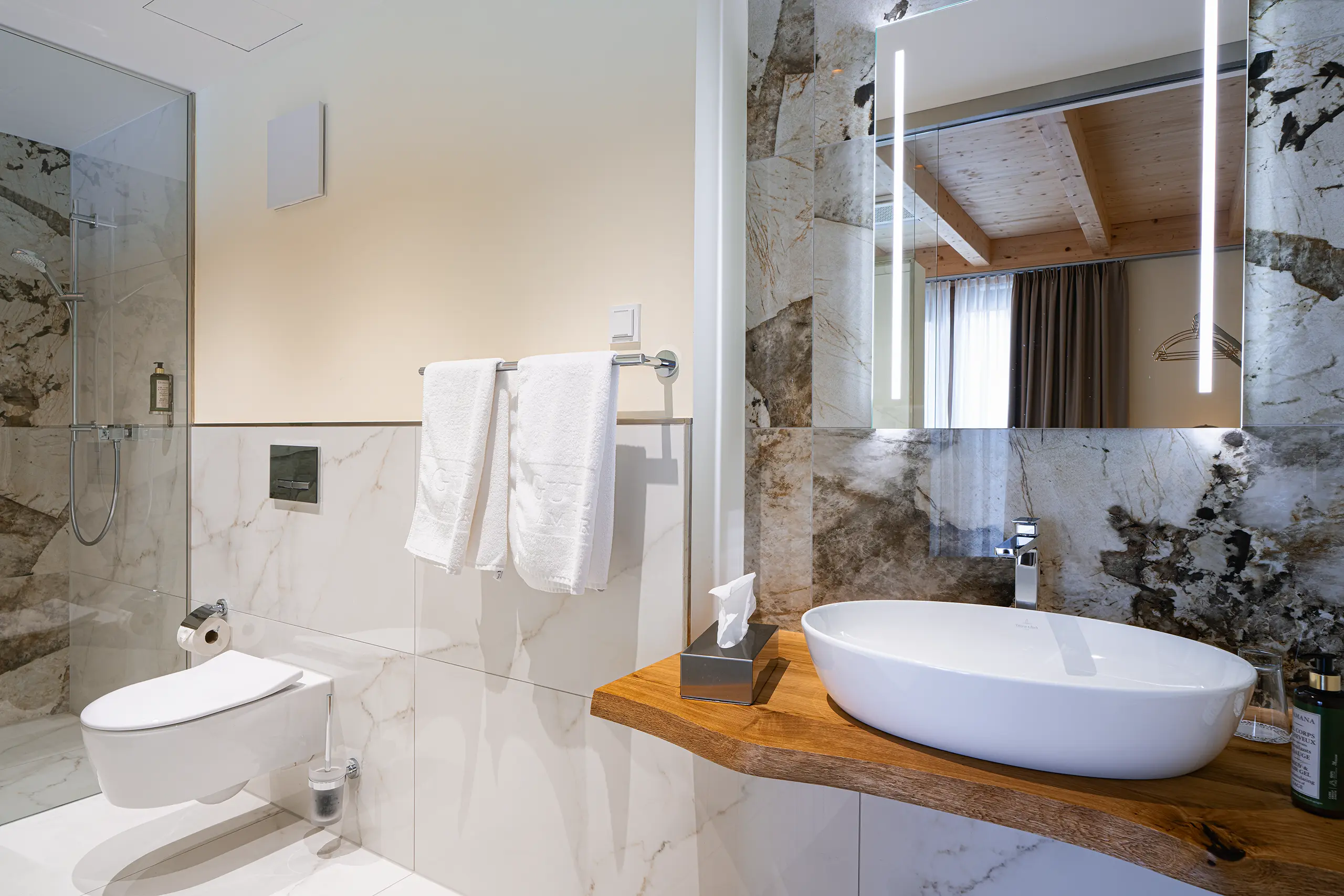 Badezimmer in Zimmer 30 im Neubau mit Waschbecken, Marmorwand und Glasdusche