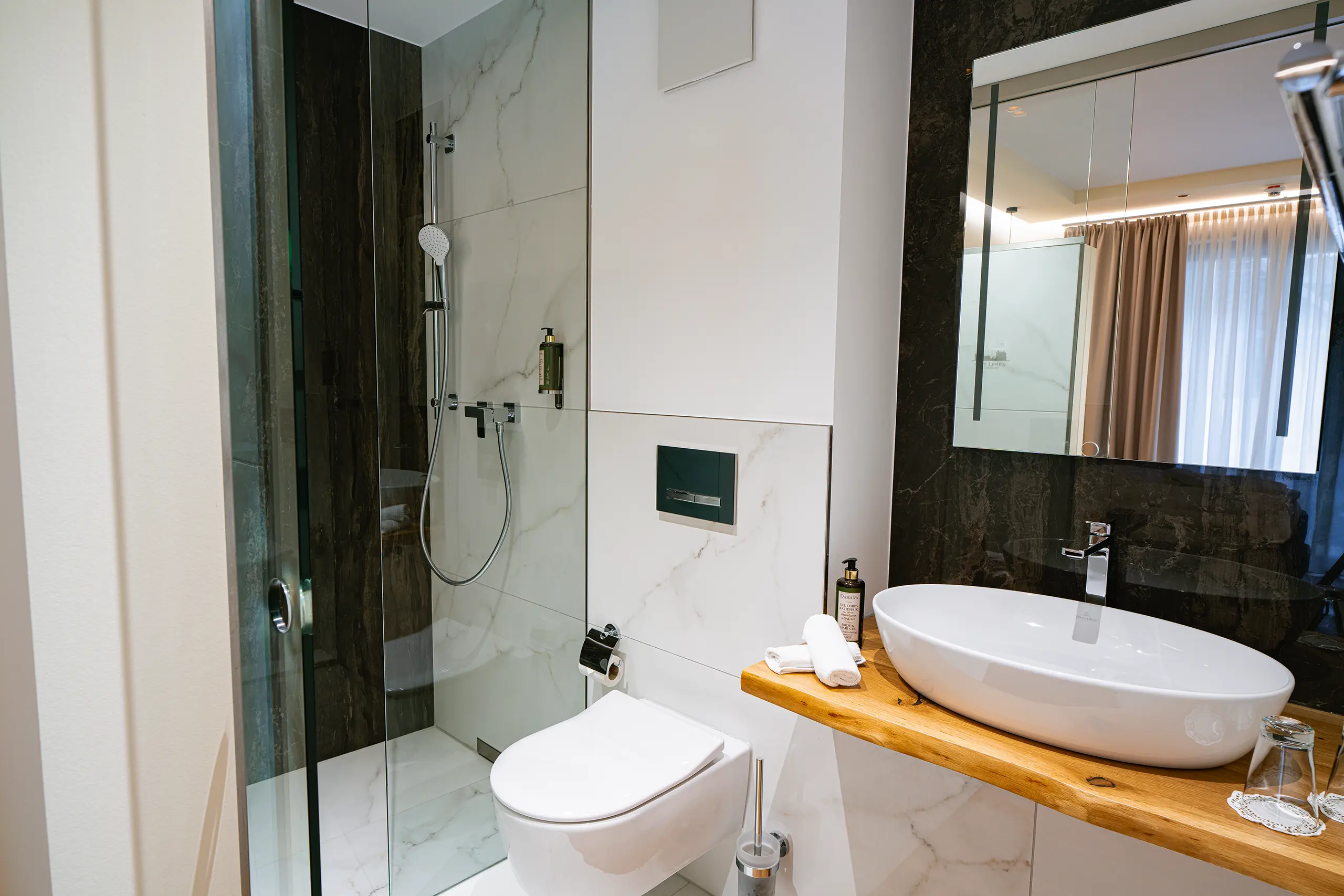 Badezimmer in Zimmer 34 im Neubau mit Waschbecken, Spiegel und dunkler Marmordusche