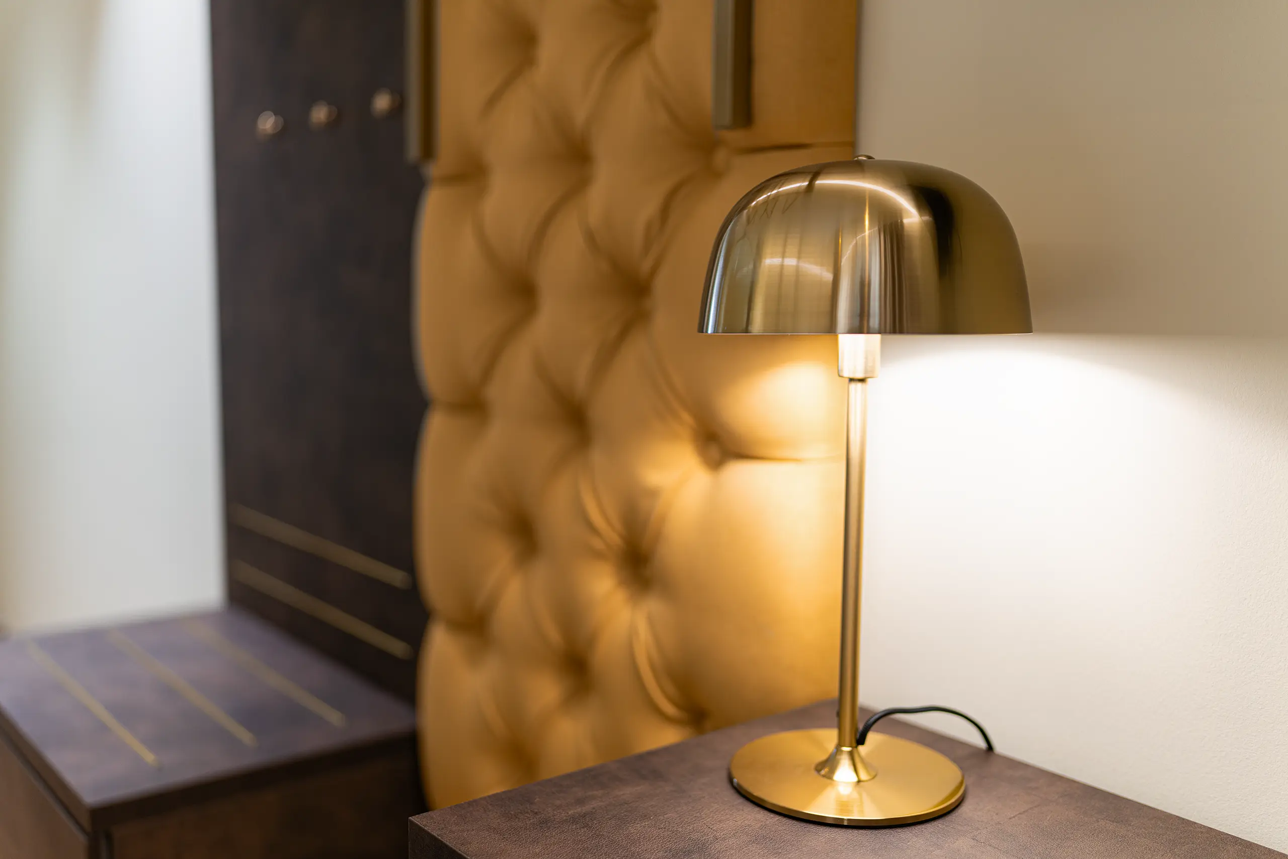 Goldene Tischleuchte auf dem Nachttisch vor gepolsterter Wand in Zimmer 35 im Neubau