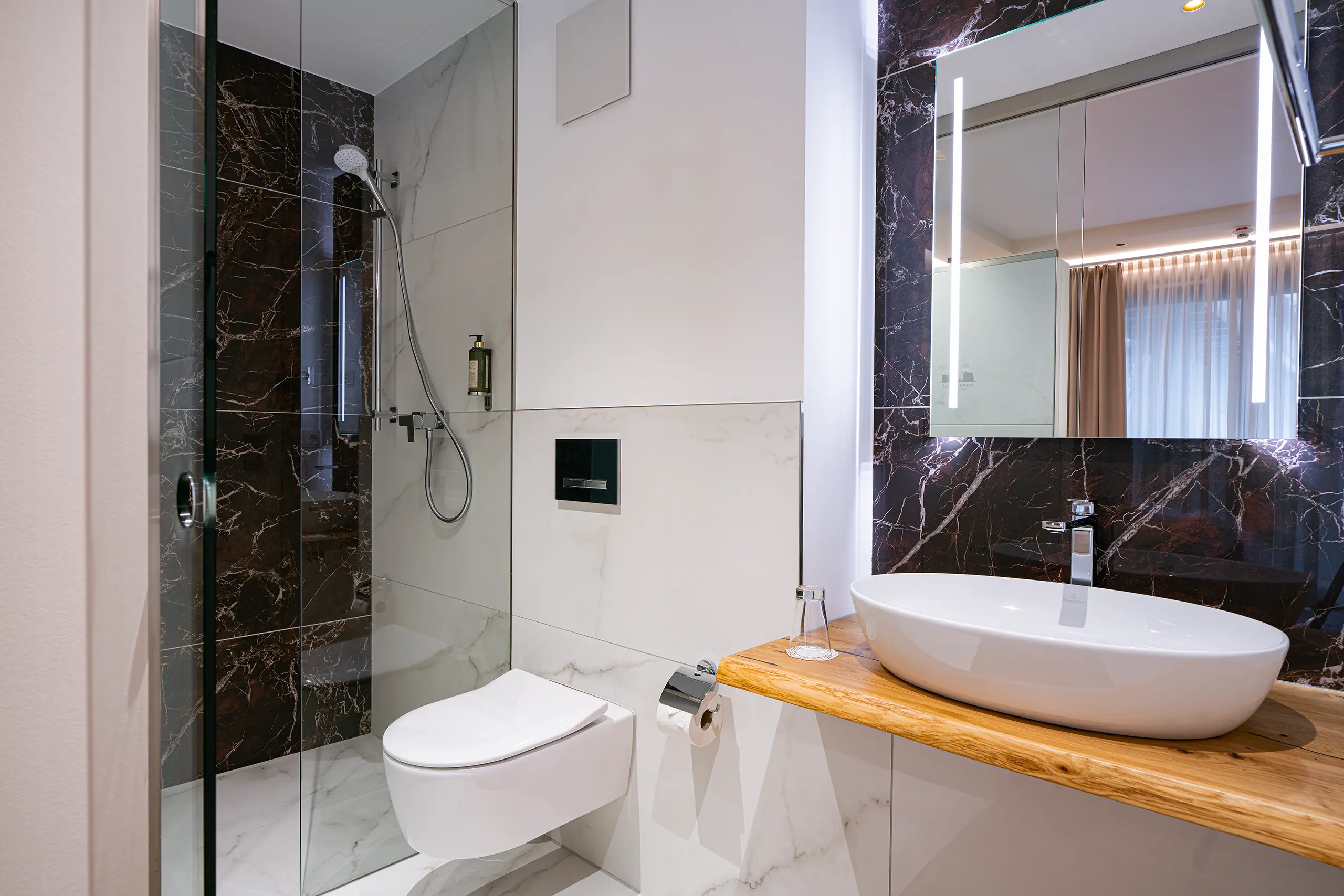 Badezimmer in Zimmer 39 im Neubau mit Waschbecken, WC und dunkler Marmordusche