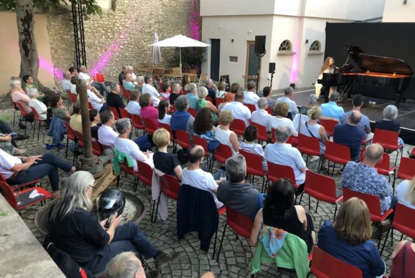Publikum auf roten Stühlen bei einem Konzert im Innenhof von Gut Leben am Morstein