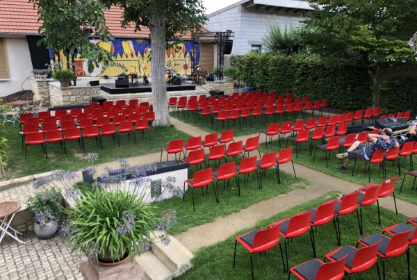 Rote Stuhlreihen und Bühne unter Bäumen für ein Open-Air-Konzert im Garten