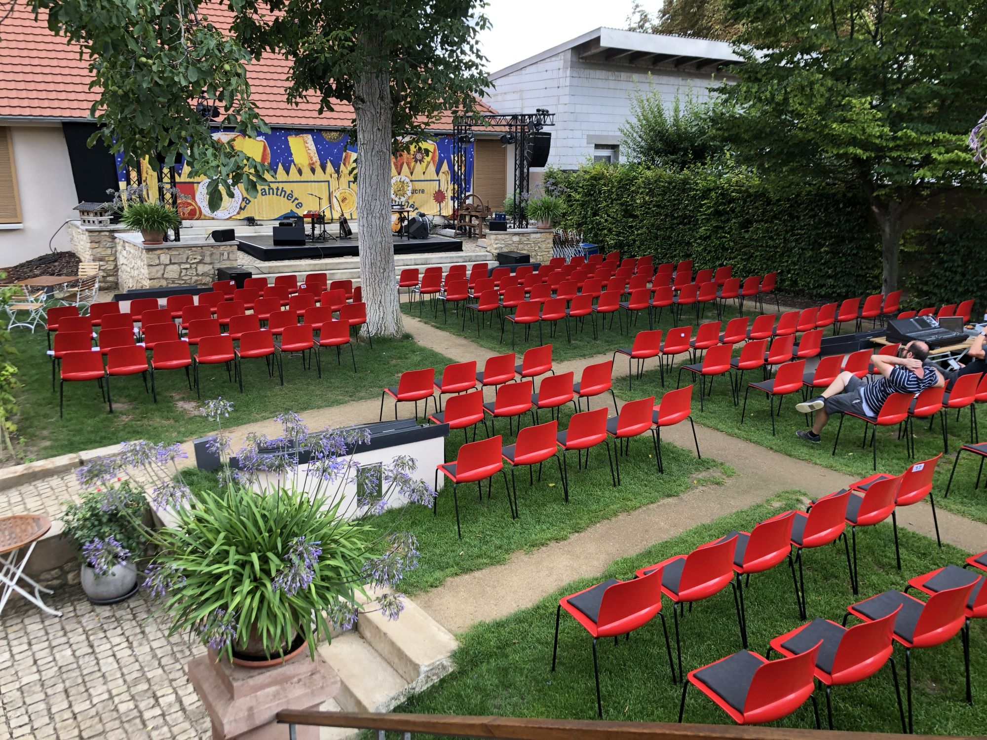 Rote Stuhlreihen und Bühne unter Bäumen für ein Open-Air-Konzert im Garten