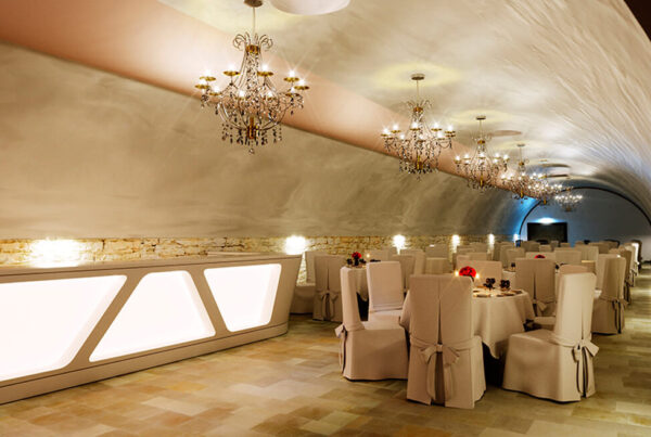 Gewölbekeller mit weißen Stuhlhussen, gedeckter Tafel und Tageslicht