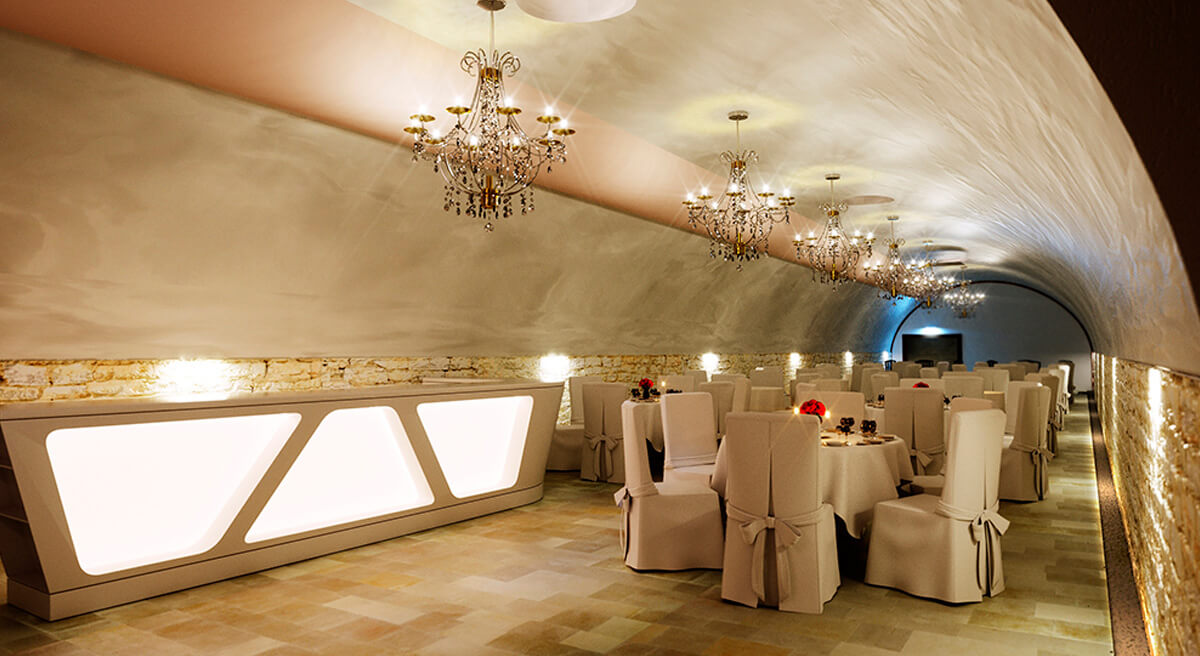 Gewölbekeller mit weißen Stuhlhussen, gedeckter Tafel und Tageslicht