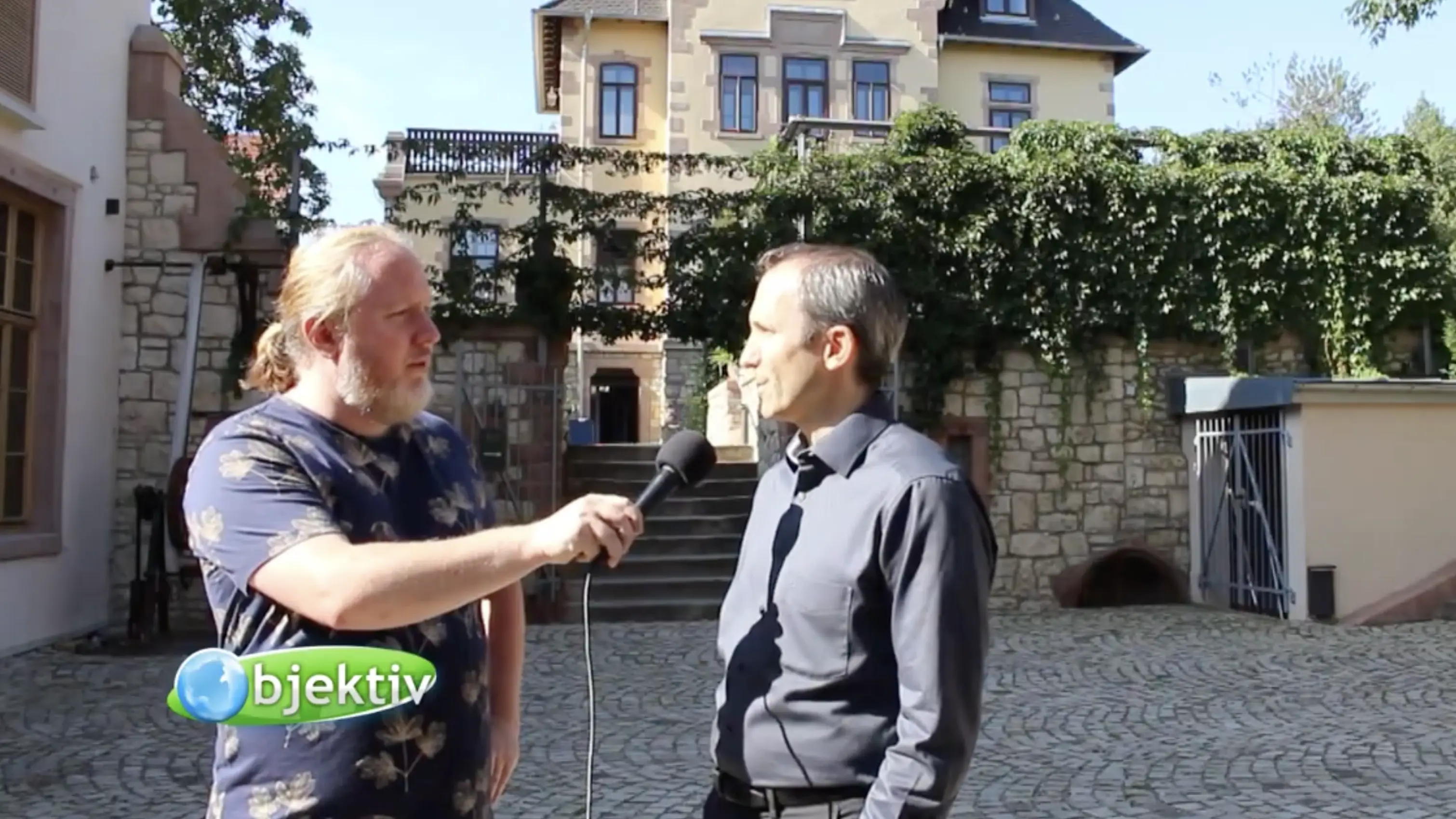 Reporter interviewt Gastgeber im Innenhof vor dem Schlösschen, Vorschaubild zum Fernsehbeitrag
